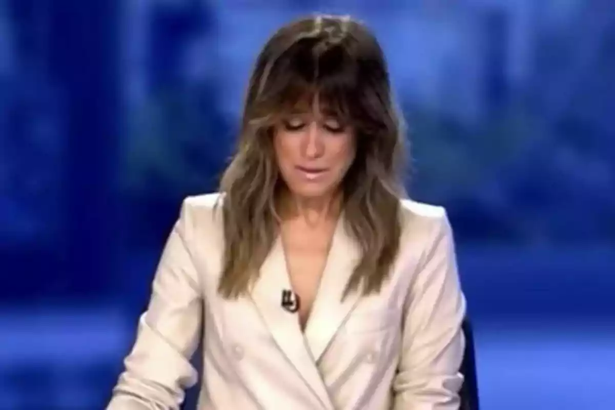 Isabel Jiménez emocionada con cabello largo y suelto, vestida con un blazer claro, en el plató de Informativos Telecinco con un fondo azul.