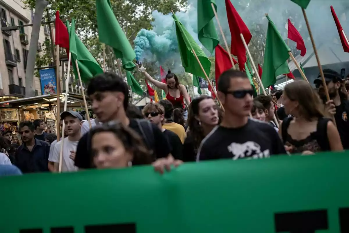 Una multitud de personas marchando con banderas verdes y rojas, mientras una mujer sostiene una bengala de humo azul.