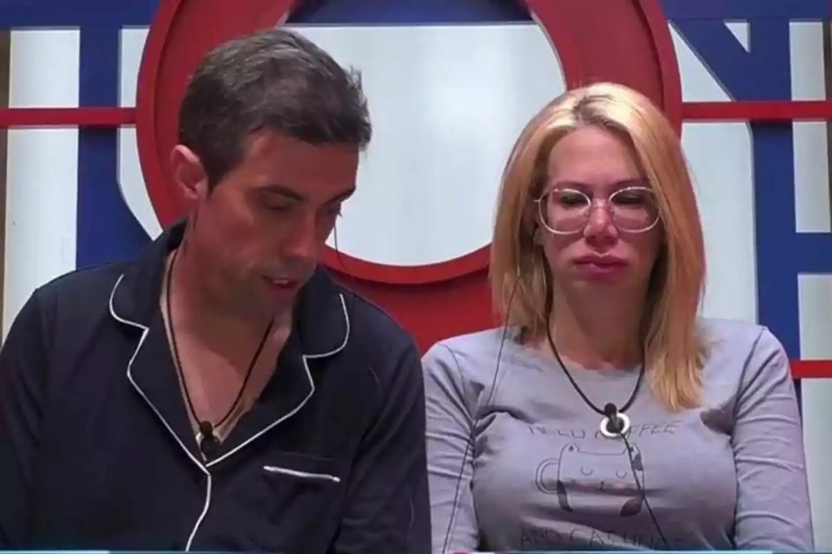 Javi y Vanessa, una mujer con gafas y un hombre con pijama oscuro, ambos con micrófonos, en el confesionario de Gran Hermano.