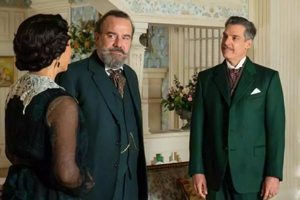 Isabel Serrano, Manuel Regueiro y Javier Mora vestidas con trajes de época conversan en una elegante sala decorada con flores y muebles antiguos en La Promesa. Isabel Serrano, Manuel Regueiro y Javier Mora vestidas con trajes de época conversan en una elegante sala decorada con flores y muebles antiguos en La Promesa.
