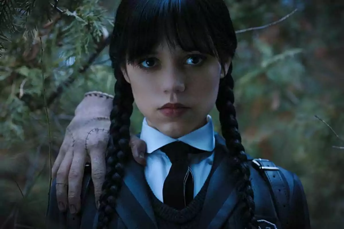 Jenna Ortega con trenzas y uniforme escolar está en un bosque con una mano sobre su hombro en Miércoles.