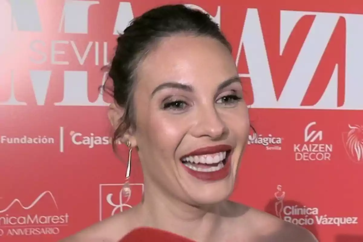Jessica Bueno sonriendo frente a un fondo rojo con logotipos y texto. Jessica Bueno sonriendo frente a un fondo rojo con logotipos y texto.