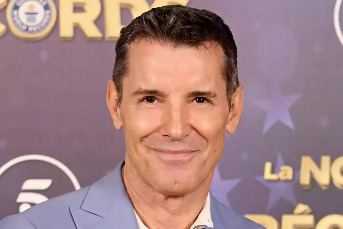 Jesús Vázquez sonriente con traje azul claro frente a un fondo con logotipos y texto de La Noche de los Récords.