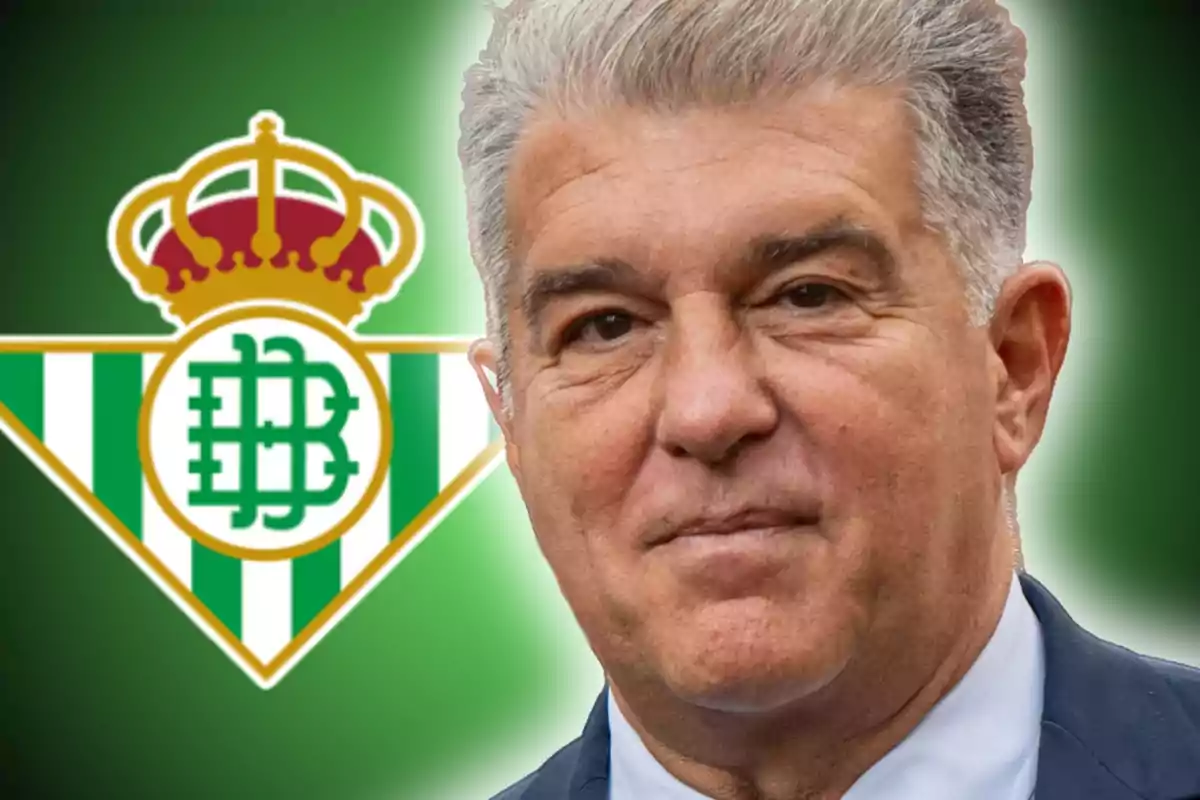 Un hombre de cabello canoso con traje frente al escudo del Real Betis.