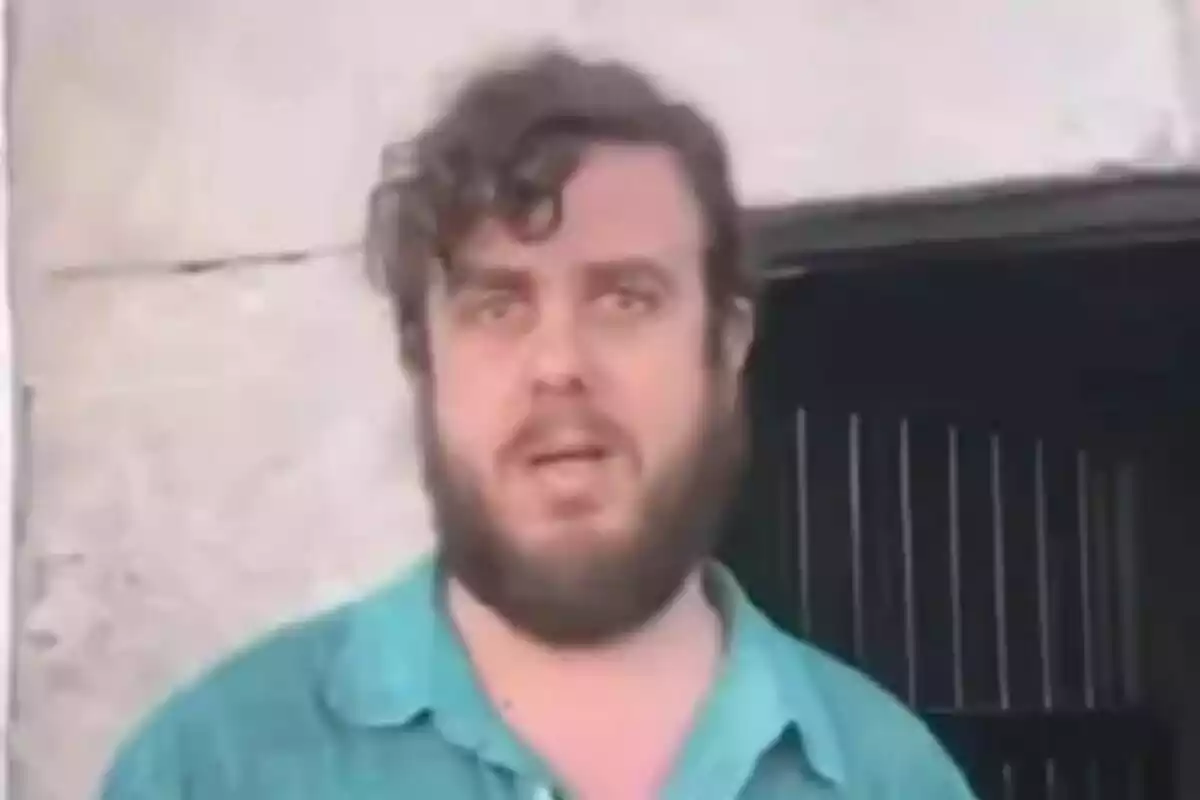 Un hombre con barba y cabello rizado está de pie frente a una pared de piedra. Un hombre con barba y cabello rizado está de pie frente a una pared de piedra.