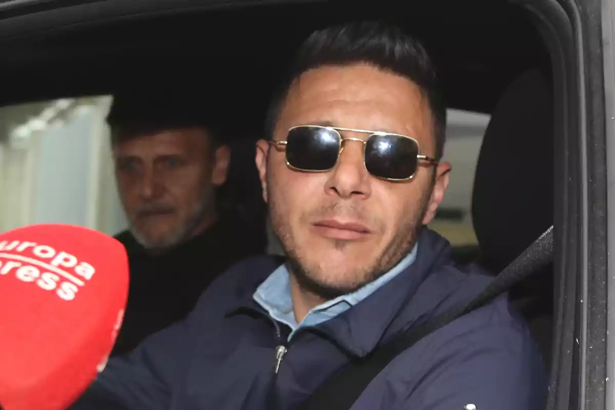 Joaquín Sánchez con gafas de sol y chaqueta azul está sentado en un automóvil junto a otra persona mientras sostiene un micrófono rojo. Joaquín Sánchez con gafas de sol y chaqueta azul está sentado en un automóvil junto a otra persona mientras sostiene un micrófono rojo.