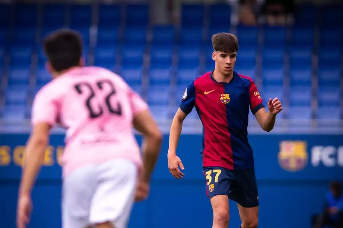 Jugador del Barcelona con el número 37 en el uniforme azul y rojo durante un partido de fútbol frente a un rival con camiseta rosa y el número 22 en un estadio con gradas azules Jugador del Barcelona con el número 37 en el uniforme azul y rojo durante un partido de fútbol frente a un rival con camiseta rosa y el número 22 en un estadio con gradas azules