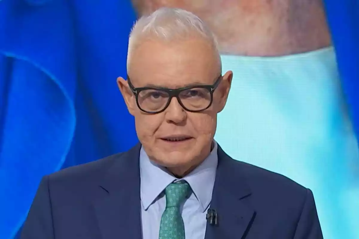 Captura de Jordi Gonzáez con cabello canoso y gafas, vestido con traje azul y corbata verde, aparece en el plató de Lazos de Sangre