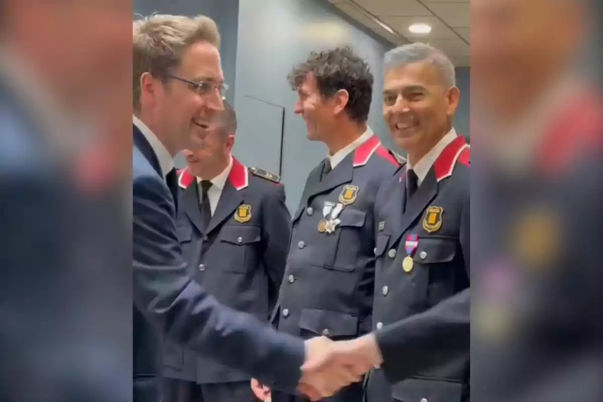 Un grupo de personas en uniforme de policía sonríe mientras una de ellas estrecha la mano de un hombre con traje. Un grupo de personas en uniforme de policía sonríe mientras una de ellas estrecha la mano de un hombre con traje.