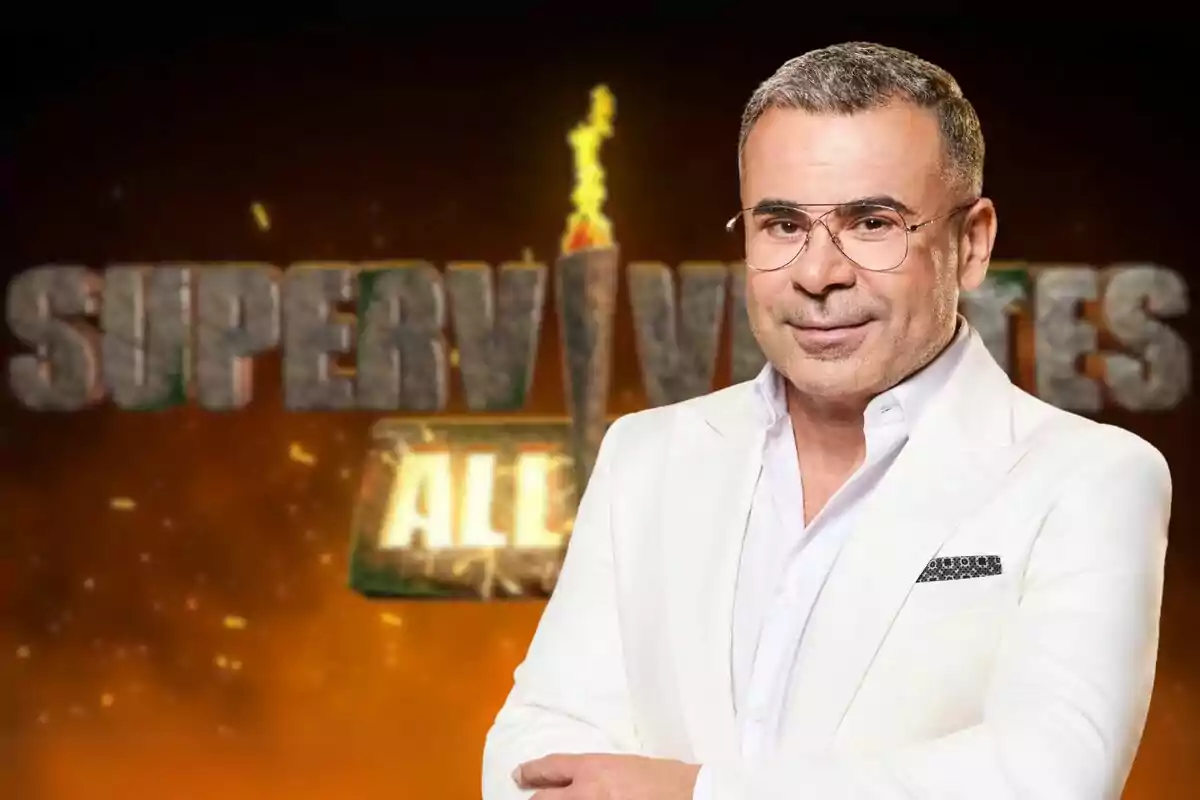 Montaje de Jorge Javier Vázquez con gafas y traje blanco posa frente a un fondo con el logotipo del programa "Supervivientes All Stars