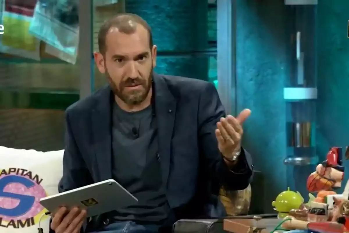 Jorge Ponce con barba y chaqueta azul sentado en 'La Revuelta' sosteniendo una tableta y gesticulando con la mano