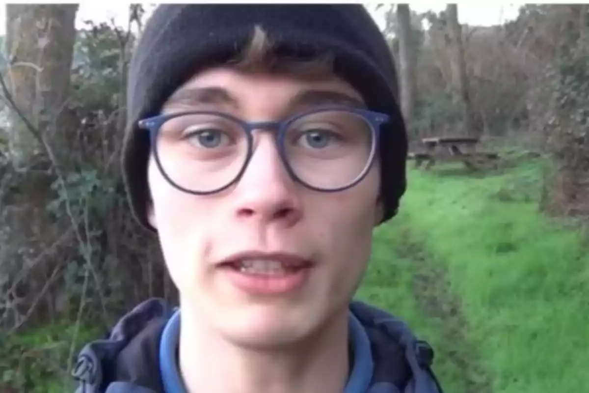 Un joven con gafas y gorro negro en un entorno natural con árboles y césped. Un joven con gafas y gorro negro en un entorno natural con árboles y césped.