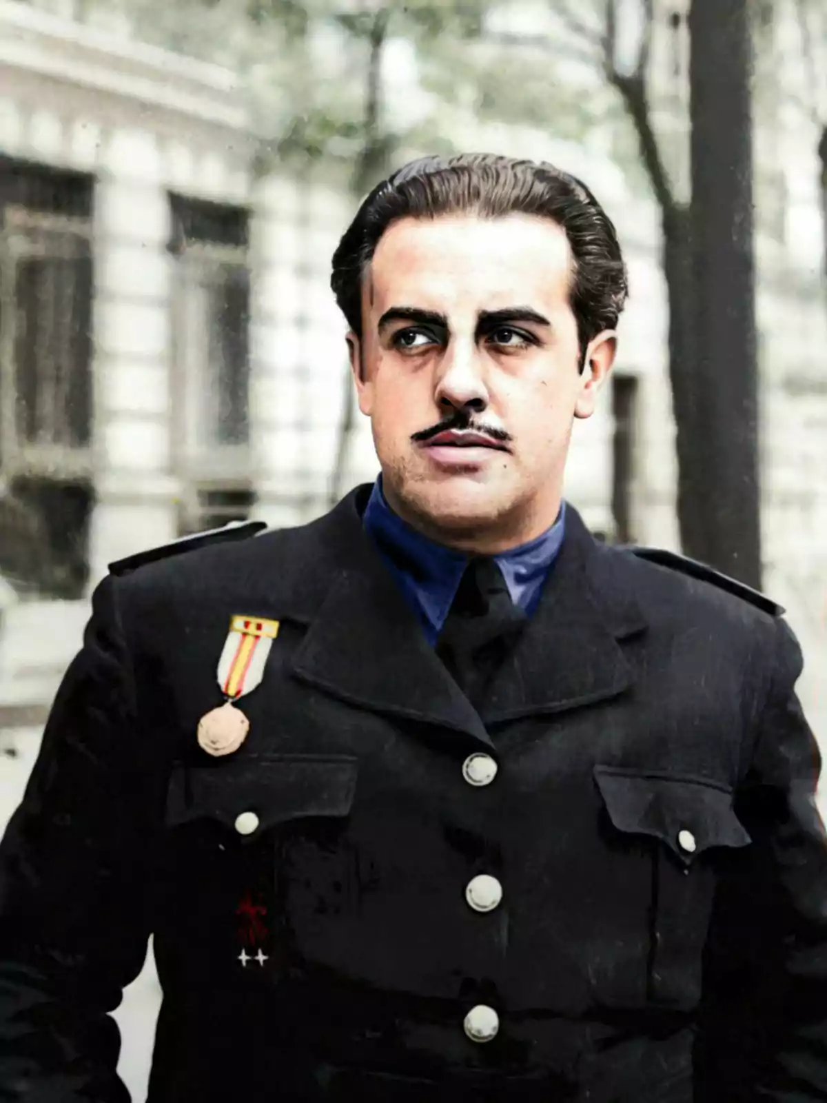 Un hombre con bigote lleva un uniforme oscuro con medallas en el pecho, posando al aire libre frente a un edificio. Un hombre con bigote lleva un uniforme oscuro con medallas en el pecho, posando al aire libre frente a un edificio.