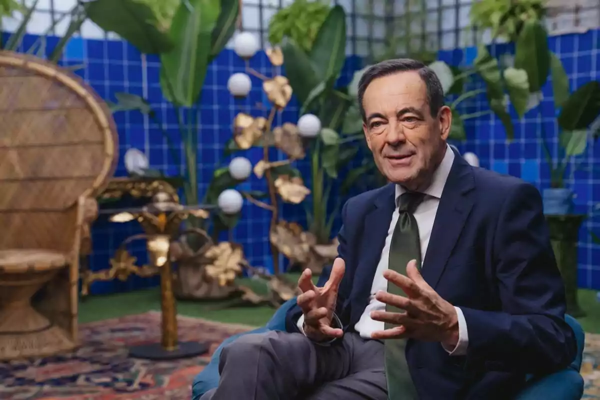 José Bono de traje oscuro y corbata verde está sentado en un sillón azul en un entorno decorado con plantas y un fondo de azulejos azules en la serie documental 'Súper Sara'. José Bono de traje oscuro y corbata verde está sentado en un sillón azul en un entorno decorado con plantas y un fondo de azulejos azules en la serie documental 'Súper Sara'.