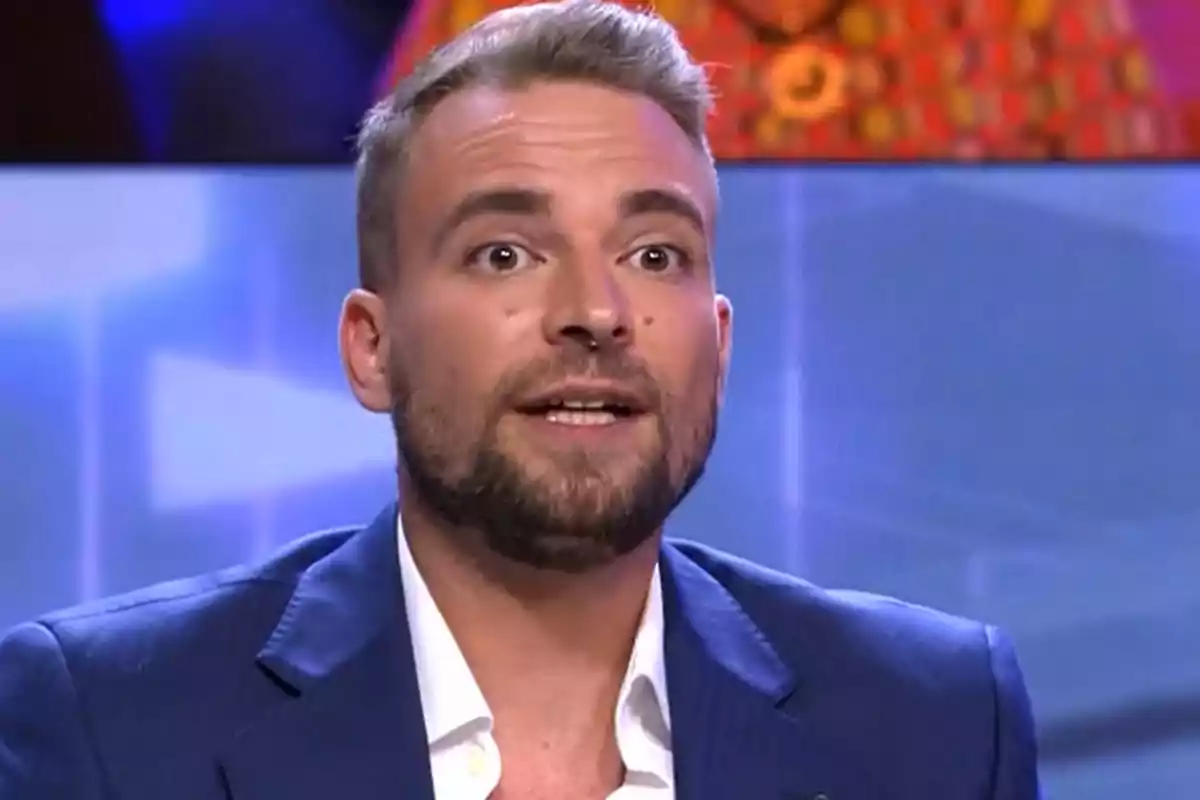 José María Almoguera, con barba y cabello corto vestido con un traje azul y camisa blanca, hablando en el plató de '¡De Viernes!'