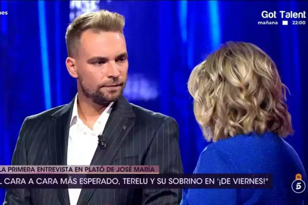 José María Almoguera con barba y traje oscuro está de pie frente a Terelu Campos de cabello rubio en el plató de De Viernes iluminado en tonos azules.