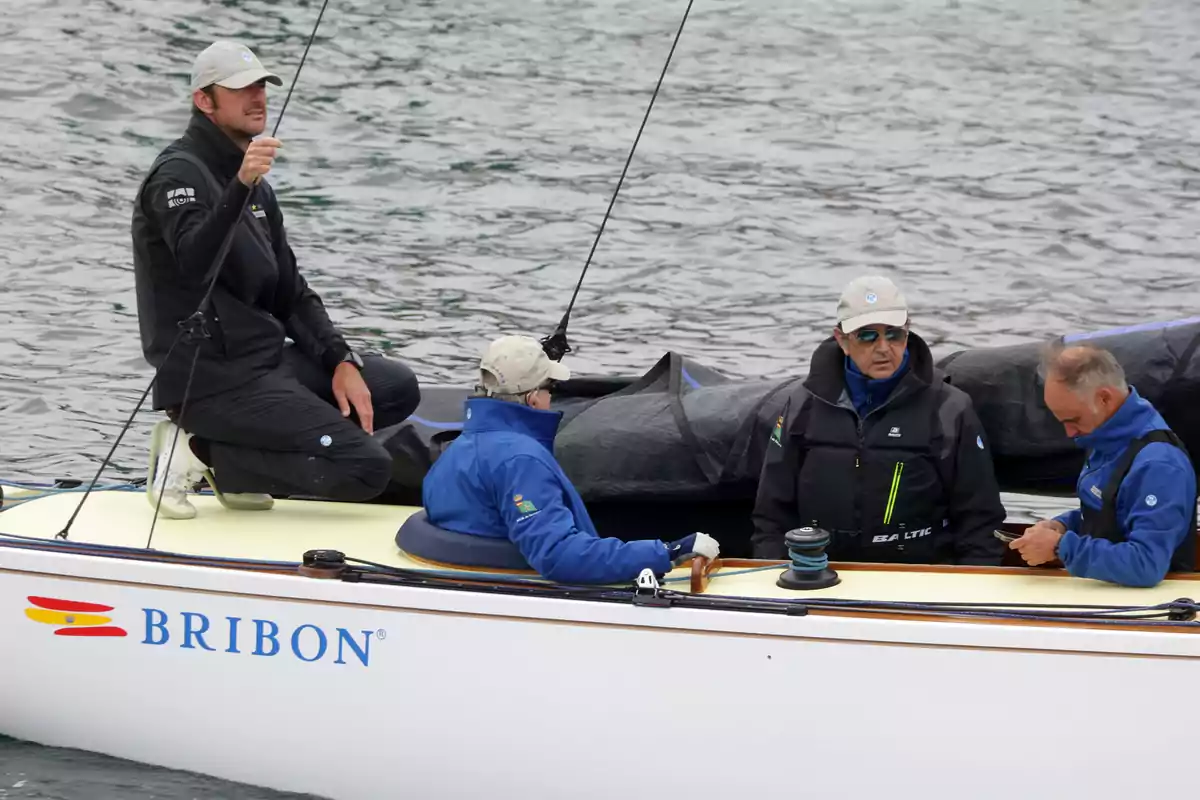 Un grupo de personas con ropa de abrigo y gorras está en un velero llamado Bribon sobre el agua. Un grupo de personas con ropa de abrigo y gorras está en un velero llamado Bribon sobre el agua.
