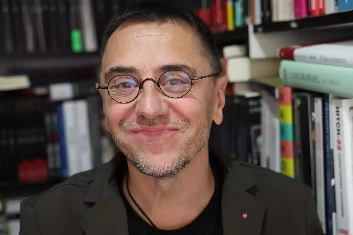 Primer plano de Juan Carlos Monedero sonriendo y de fondo una estantería con libros