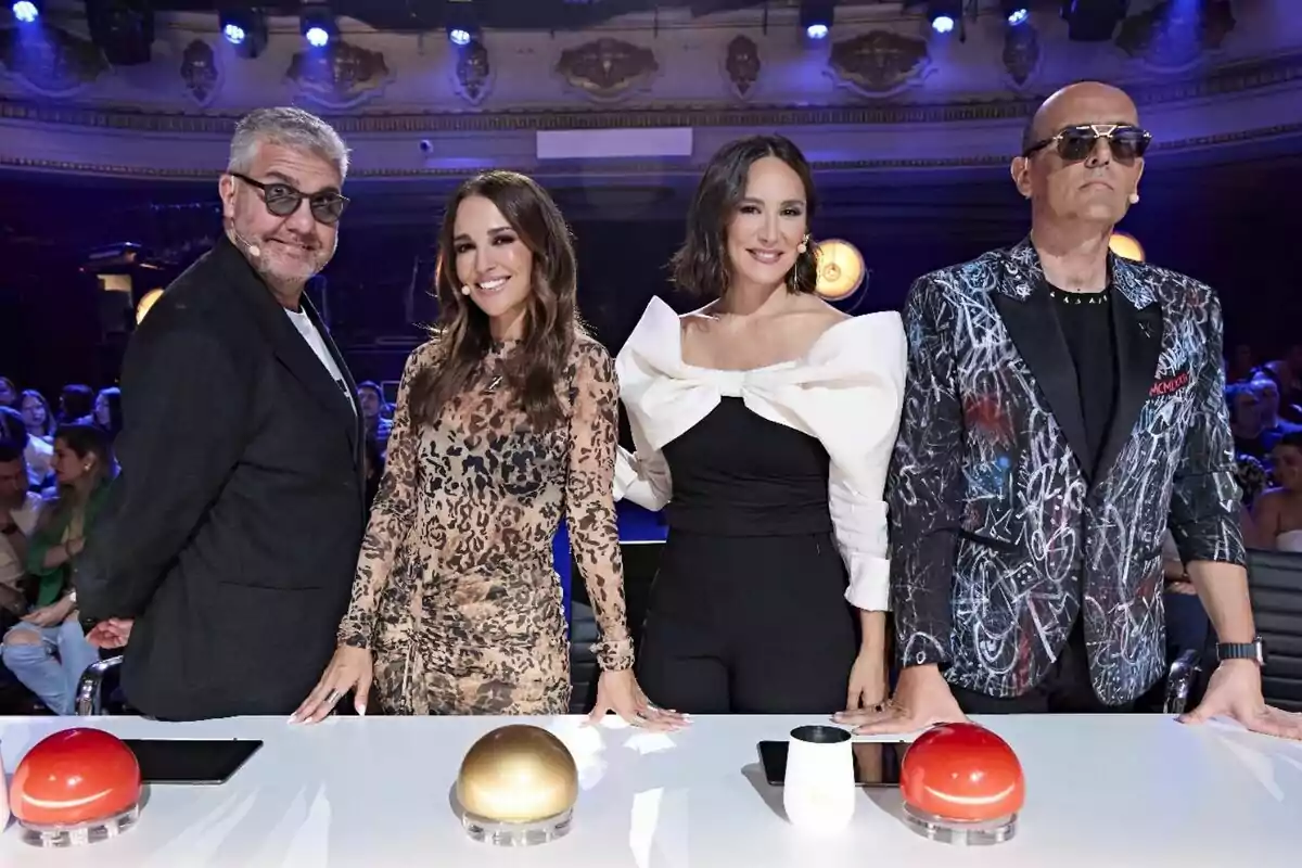 Risto Mejide, Paula Echevarría, Tamara Falcó y Florentino Fernández posan juntos detrás de una mesa con botones de colores en un escenario iluminado de Got Talent.