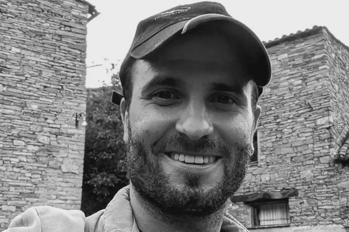 Fotografía de Julián ortega con barba y gorra sonríe frente a una construcción de piedra en El Pueblo