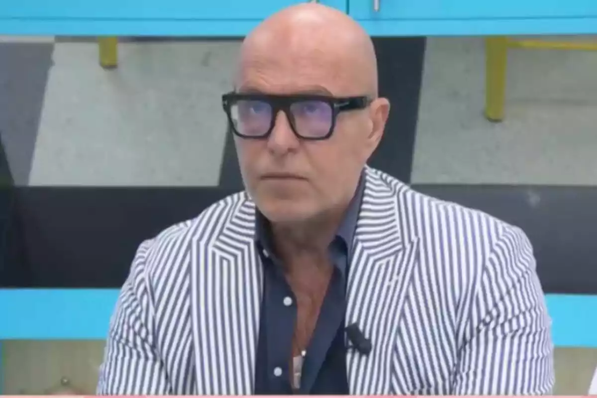 Kiko Matamoros calvo con gafas y saco de rayas blancas y azules sentado en un ambiente interior en 'La familia de la tele'.