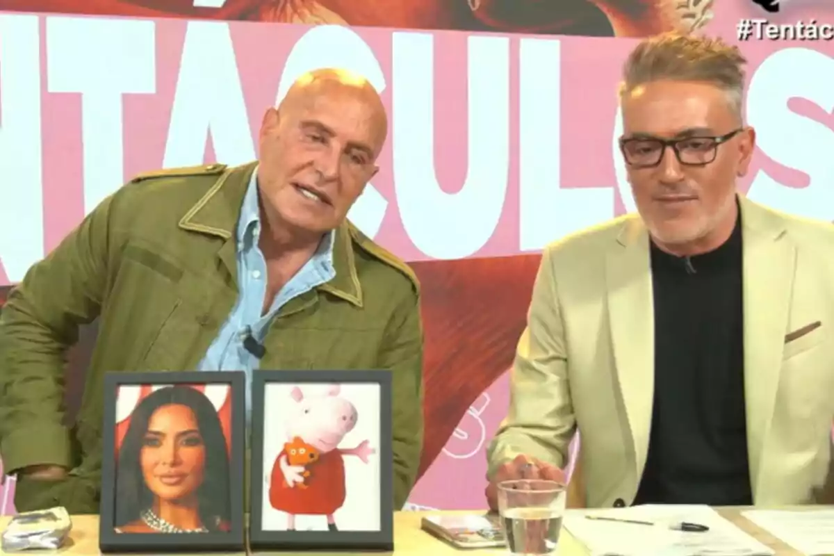 Kiko Matamoros y Kiko Hernández están sentados en un set de televisión con un fondo que dice "TENTÁCULOS" y en la mesa frente a ellos hay dos marcos con imágenes, una de una mujer y otra de un personaje animado.