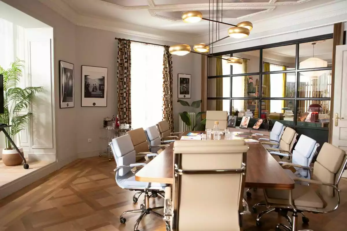 Una sala de reuniones elegante con una mesa de madera rodeada de sillas de oficina, decorada con plantas, cuadros en las paredes y una lámpara moderna en el techo en 'La Agencia'. Una sala de reuniones elegante con una mesa de madera rodeada de sillas de oficina, decorada con plantas, cuadros en las paredes y una lámpara moderna en el techo en 'La Agencia'.