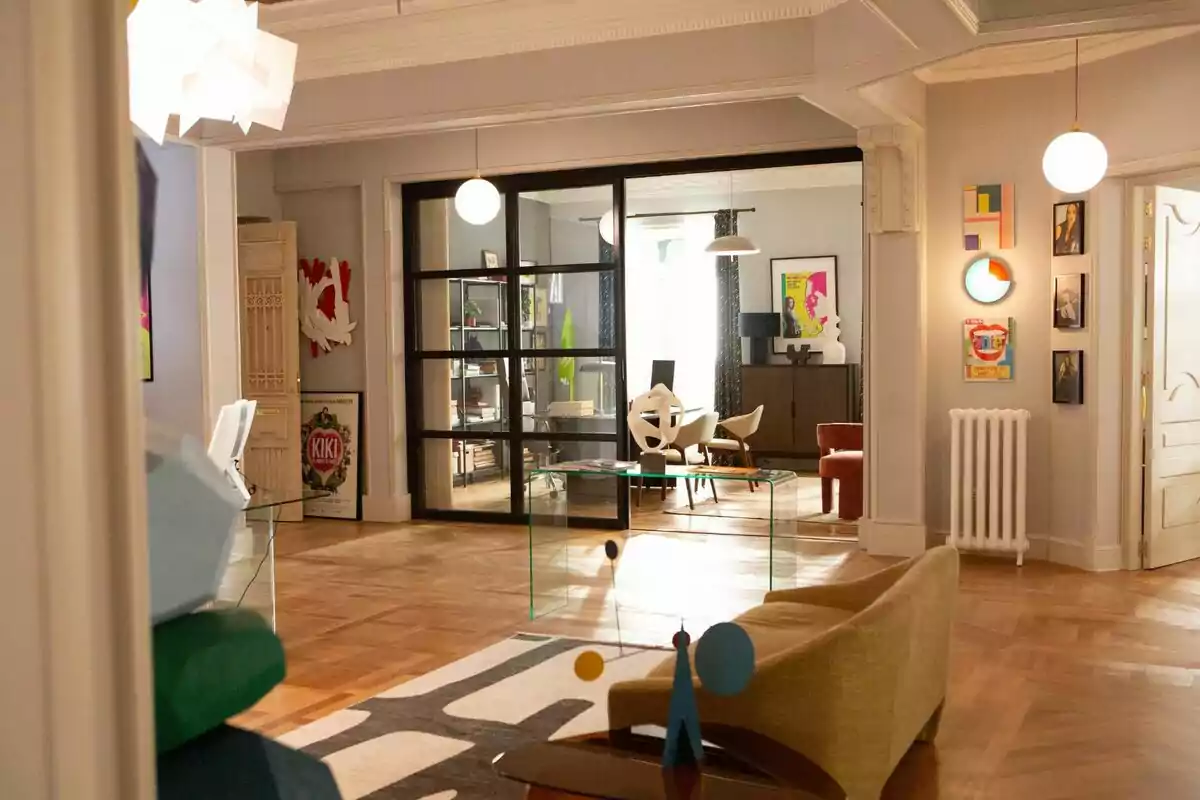 Una sala de estar moderna con muebles de diseño, arte en las paredes y una puerta de vidrio que separa dos espacios. Set de rodaje de 'La Agencia'. Una sala de estar moderna con muebles de diseño, arte en las paredes y una puerta de vidrio que separa dos espacios. Set de rodaje de 'La Agencia'.