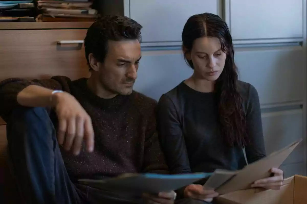 Milena Smit y Miki Esparbé sentadas en el suelo revisando documentos con expresión seria en La chica de nieve.