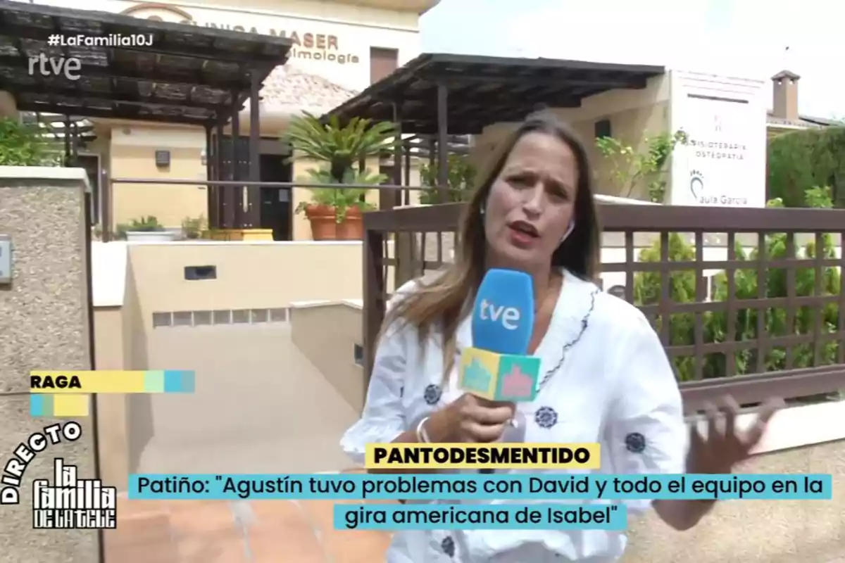 Amanda Párraga sosteniendo un micrófono azul de tve mientras informa en directo frente a un edificio con plantas y carteles de clínicas, con gráficos y subtítulos en la pantalla. Captura de 'la Familia de la Tele' Amanda Párraga sosteniendo un micrófono azul de tve mientras informa en directo frente a un edificio con plantas y carteles de clínicas, con gráficos y subtítulos en la pantalla. Captura de 'la Familia de la Tele'