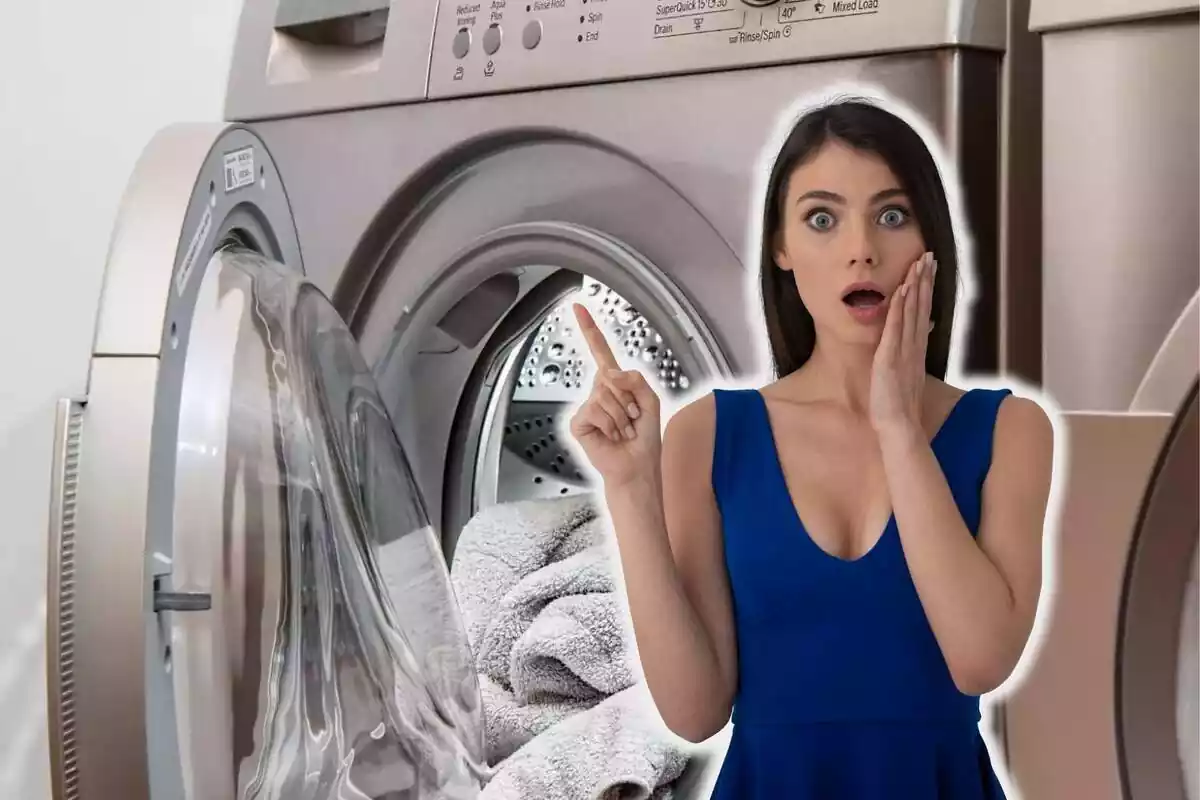 Mujer morena con camiseta azul, sorprendida y señalando con el índice hacia arriba, sobre fondo de primer plano de lavadora metalizada abierta con toalla blanca dentro