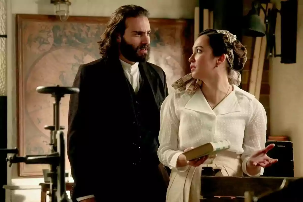 Catalina y Adriano vestidos con ropa de época conversan en una habitación con un mapa antiguo en la pared. Captura de 'La Promesa' Catalina y Adriano vestidos con ropa de época conversan en una habitación con un mapa antiguo en la pared. Captura de 'La Promesa'