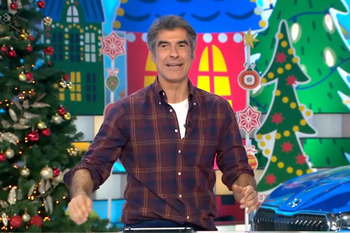 Jorge Fernández de pie con camisa a cuadros en un set decorado con motivos navideños y un árbol de Navidad. Captura de 'La Ruleta de la Suerte'