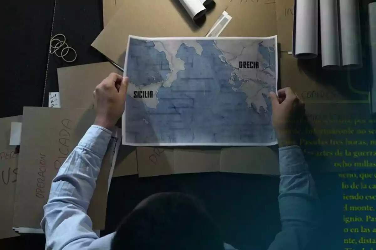 Persona observando un mapa de Sicilia y Grecia sobre una mesa llena de carpetas y documentos de laSexta Columna.