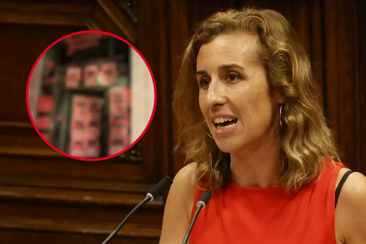 Laia Estrada, vestida con una blusa roja, habla frente a un micrófono en un entorno de madera oscura; en la esquina superior izquierda de la imagen hay un círculo rojo que muestra una escena borrosa.