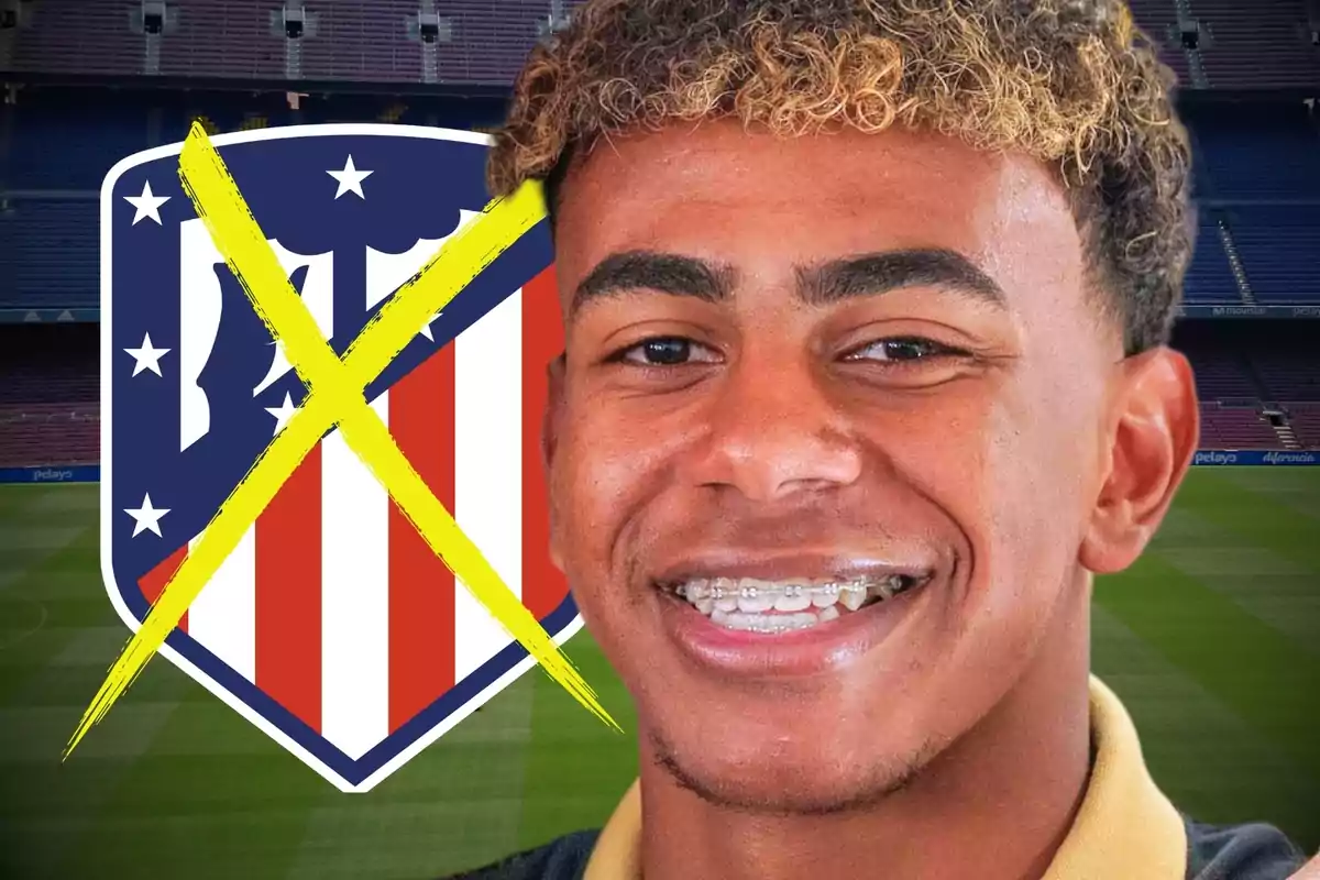 Un joven sonriente con brackets frente a un escudo del Atlético de Madrid tachado con una X amarilla en un estadio de fútbol.