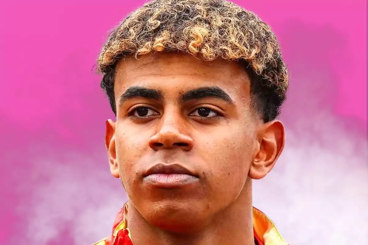 Un joven con cabello rizado y teñido de rubio en las puntas, con una expresión seria, sobre un fondo rosa.
