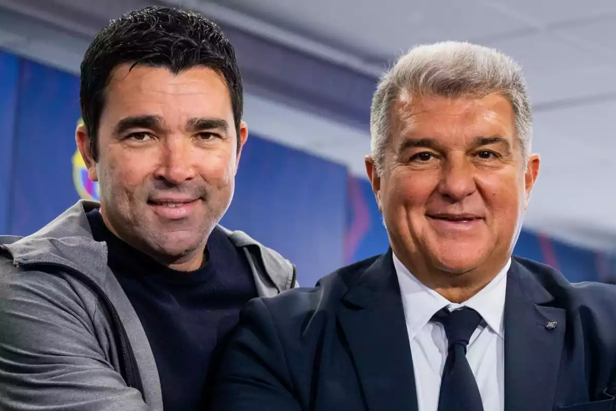 Dos hombres posando juntos, uno con una chaqueta gris y camiseta negra, y el otro con un traje oscuro y corbata. Están en un entorno interior con un fondo desenfocado que parece tener colores azul y rojo. Ambos están sonriendo y mirando hacia la cámara.