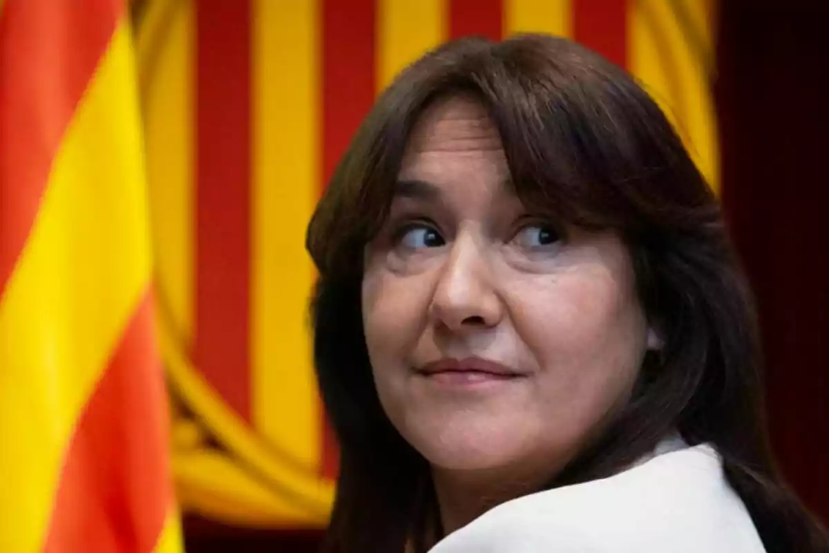 Mujer de cabello castaño mira hacia un lado con una bandera de fondo en tonos rojos y amarillos