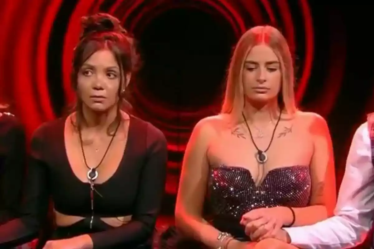 Laura Galera y Daniela sentadas en la sala de expulsión de Gran Hermano con luces rojas de fondo, una lleva un vestido negro y la otra un vestido brillante.