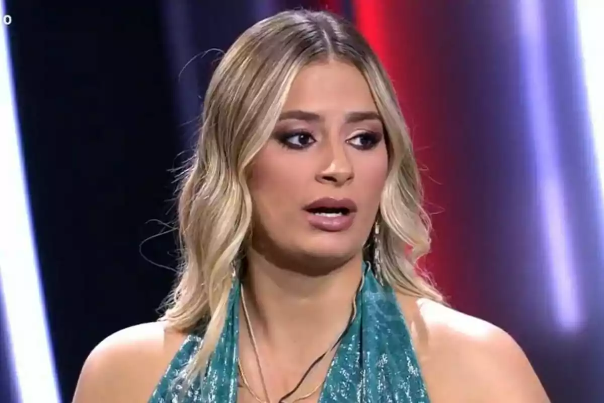 Laura Galera con cabello rubio y vestido azul en un entorno iluminado en el plató de Gran Hermano.