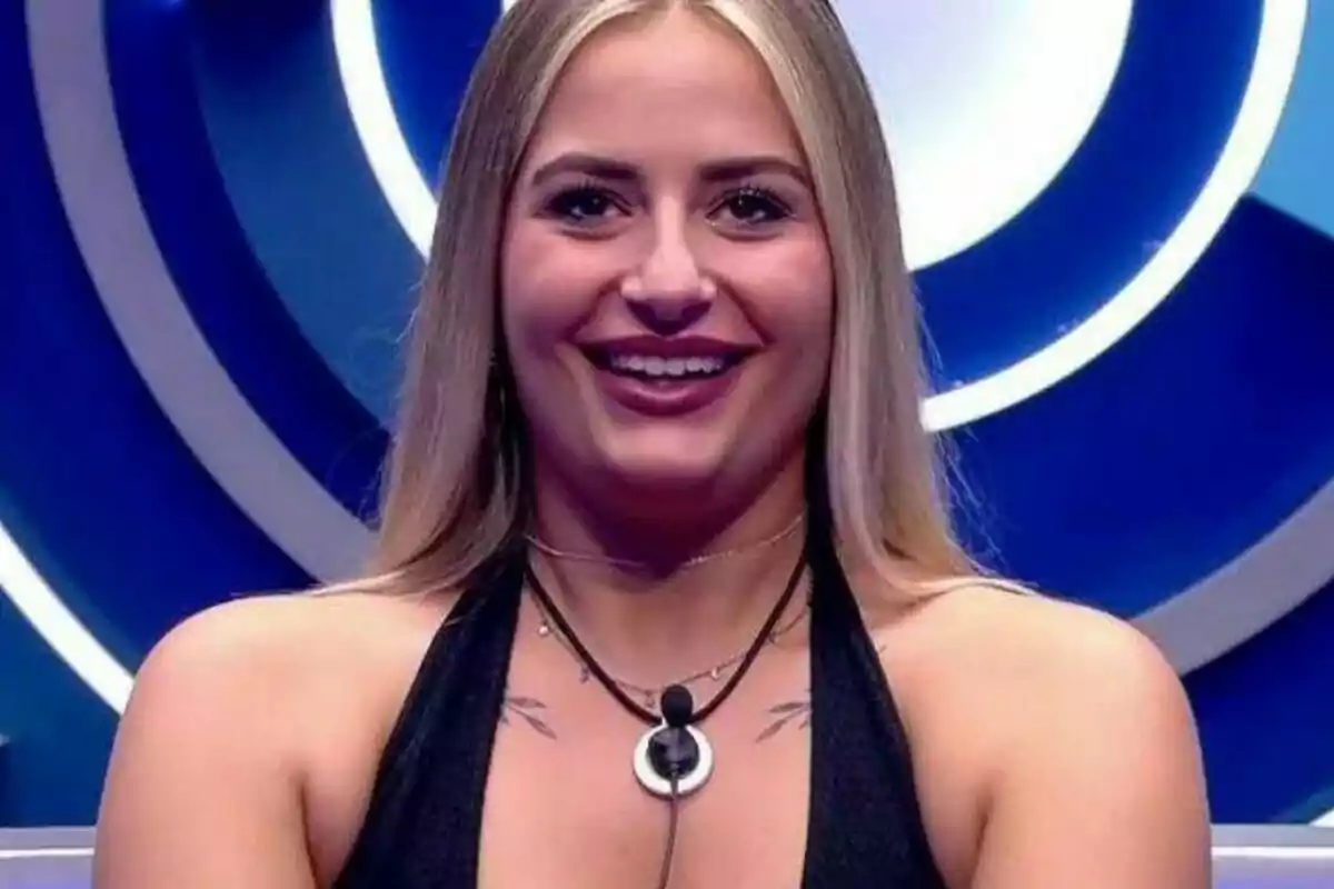 Laura Galera rubia sonríe frente a una cámara con un fondo azul y blanco en el confesionario de Gran Hermano.