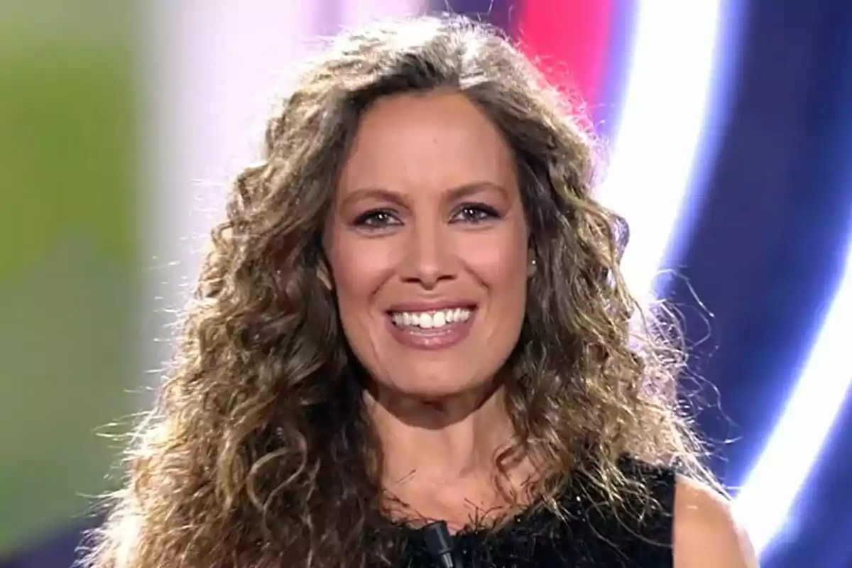 Laura Madrueño con cabello rizado y sonrisa en un entorno iluminado en el plató de Gran Hermano.