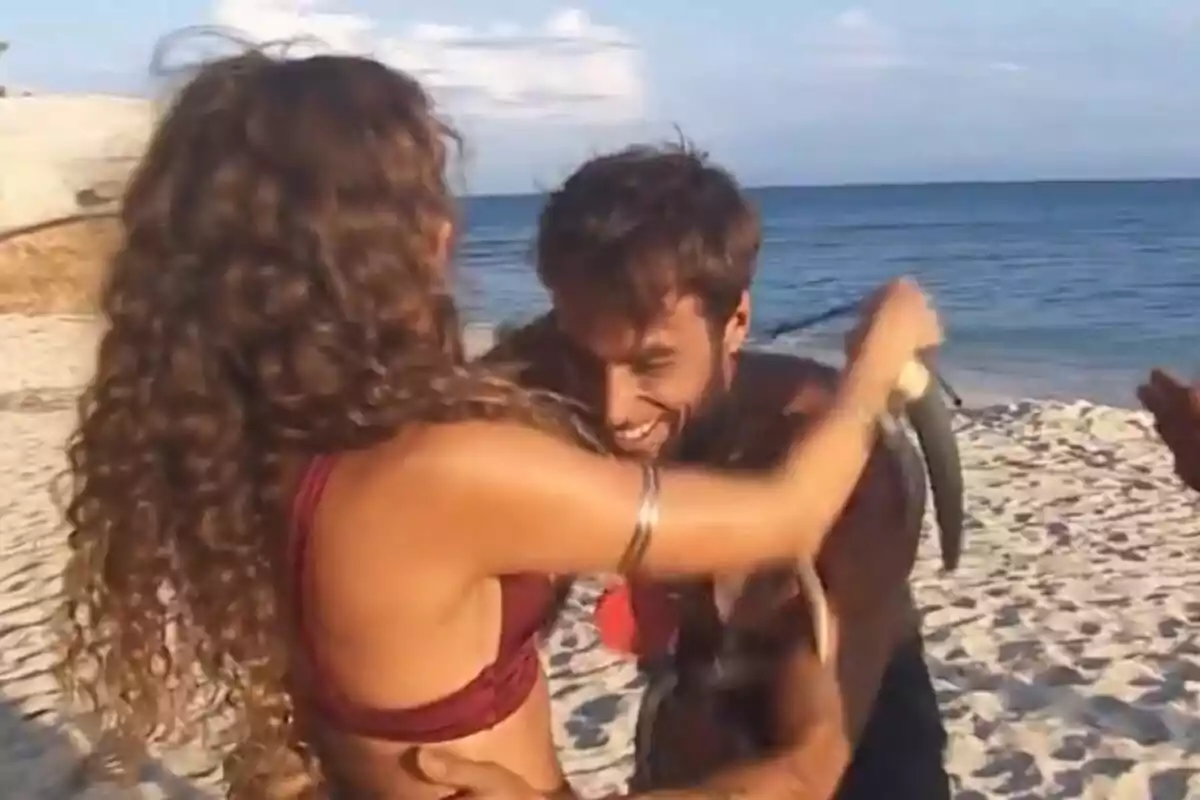 Laura Madrueño y Montoya sonrientes se abraza en la playa mientras el hombre sostiene un pez en Supervivientes.