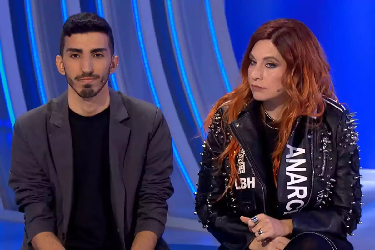 Leire Martínez y un chico sentadas en Hay en una cosa que te quiero decir con fondo azul, una de ellas lleva una chaqueta de cuero con tachuelas y la otra viste un blazer oscuro. Leire Martínez y un chico sentadas en Hay en una cosa que te quiero decir con fondo azul, una de ellas lleva una chaqueta de cuero con tachuelas y la otra viste un blazer oscuro.