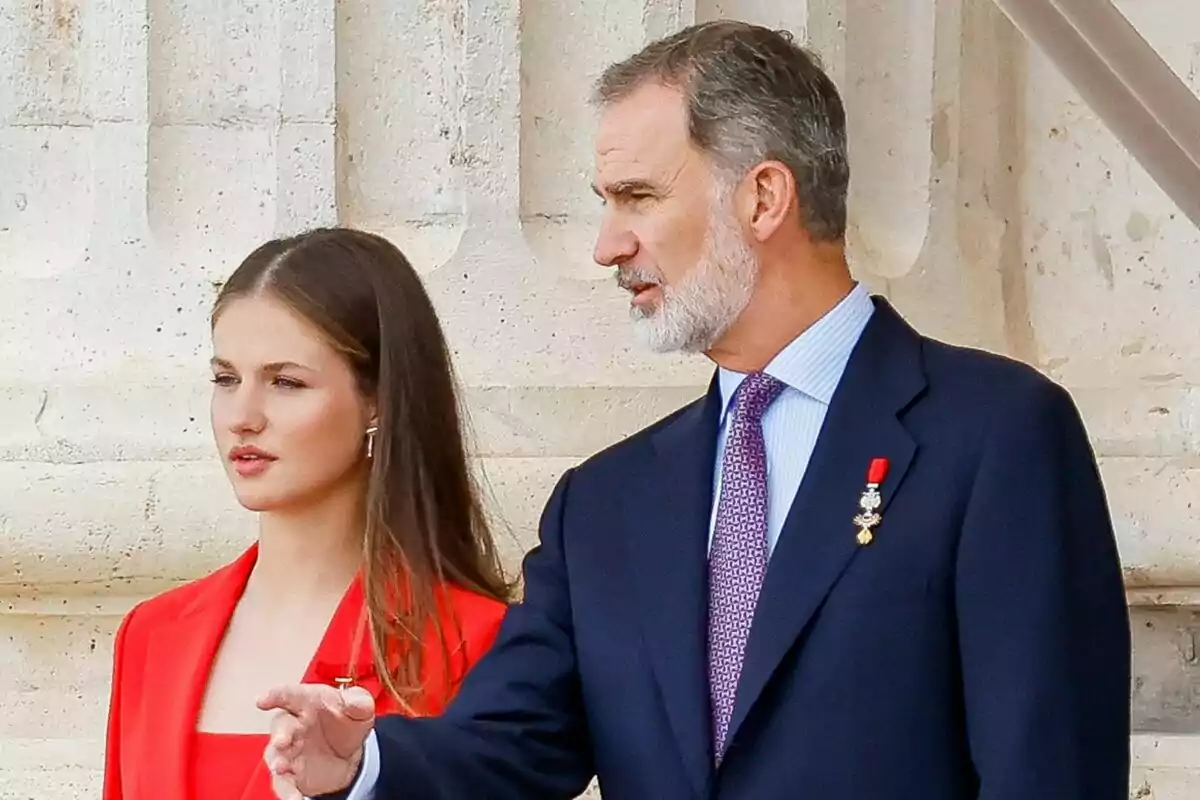 Leonor seria en traje rojo junto a Felipe VI serio señalando en traje azul