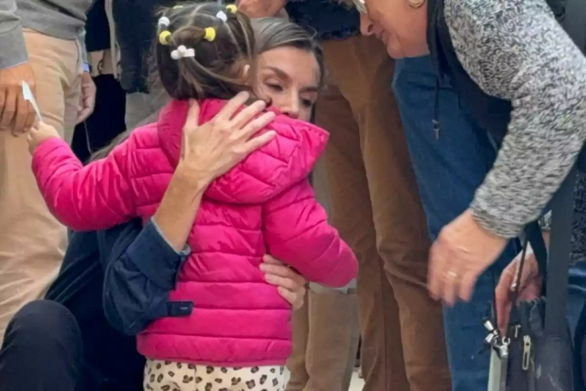 Letizia abraza a una niña que lleva una chaqueta rosa mientras otras personas observan.