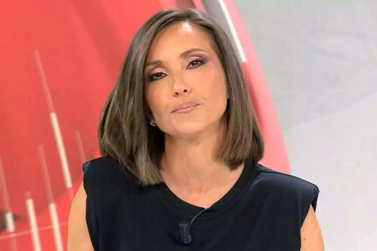 Lidia Camón con cabello corto y castaño, vestida con una camiseta negra, está frente a un fondo rojo y gris en Noticias Cuatro.