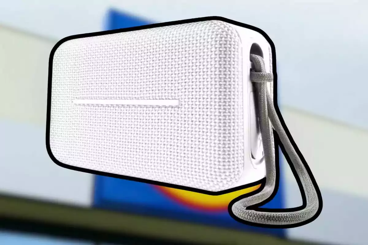 Alt: Altavoz portátil blanco con textura de tela y una correa gris. Alt: Altavoz portátil blanco con textura de tela y una correa gris.