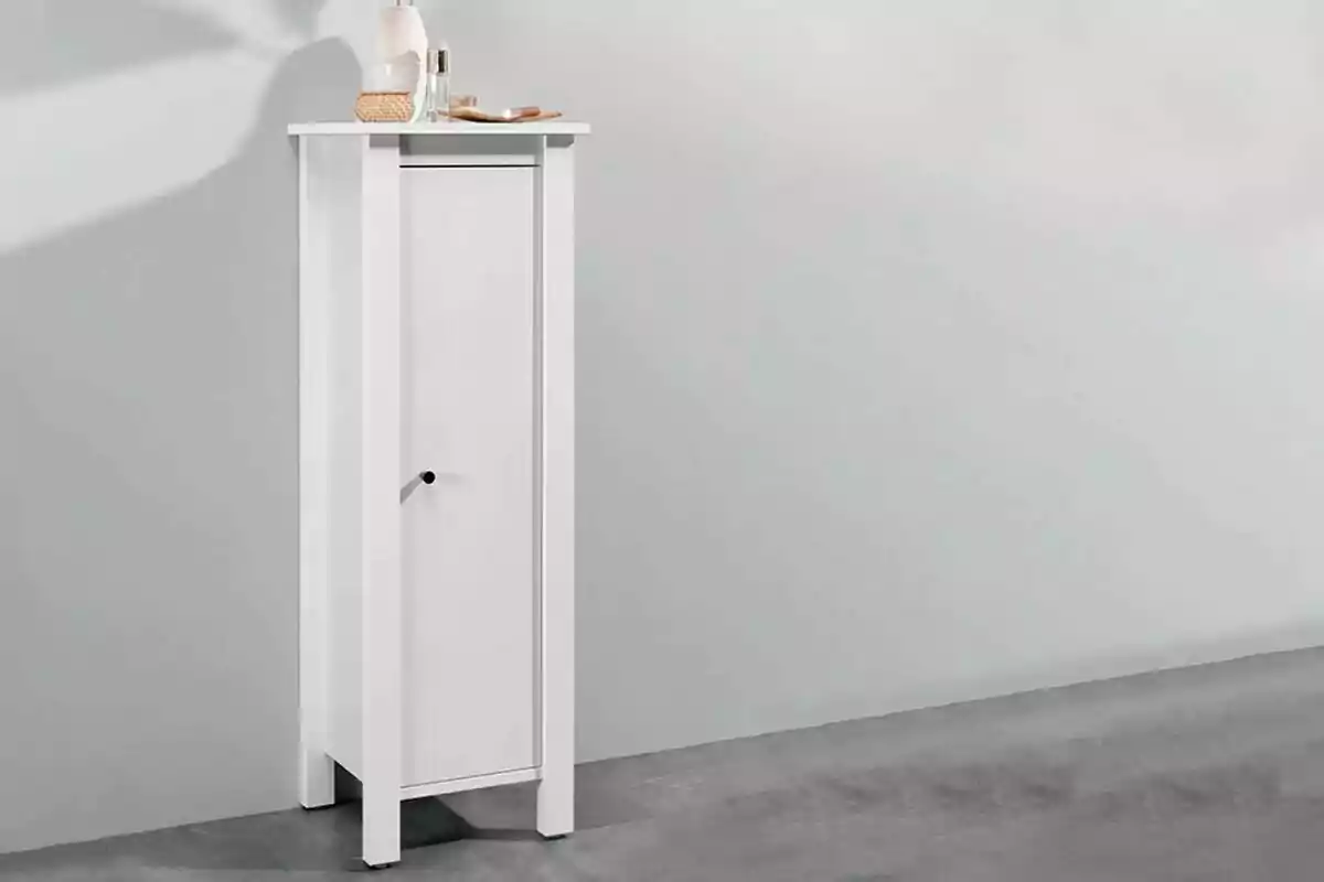 Un mueble blanco alto y estrecho con una puerta y algunos objetos decorativos en la parte superior. Un mueble blanco alto y estrecho con una puerta y algunos objetos decorativos en la parte superior.